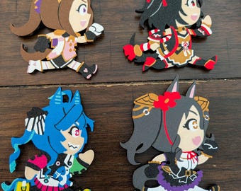 May include: Four flat, stylized character charms featuring anime-inspired figures in dynamic running poses. The top left figure has brown hair, the top right has black hair with red accents, the bottom left has blue hair, and the bottom right has dark hair with a red flower accessory.