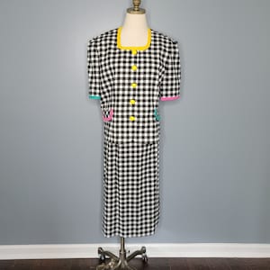 May include: A black and white gingham dress suit with yellow, pink, and teal trim. The dress has a square neckline and short sleeves. The skirt is knee-length.