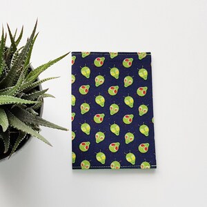May include: A dark blue fabric passport holder with a repeating pattern of green alien faces. The alien faces have red and yellow details.