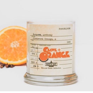 Peut inclure: Un bocal en verre pour bougie avec une &eacute;tiquette qui indique "Clove + Orange" et "Banned Books Collection". L'&eacute;tiquette est stylis&eacute;e comme une carte de biblioth&egrave;que avec le titre du livre "Clockwork Orange" d'Anthony Burgess.