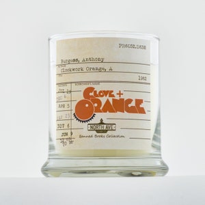 Peut inclure: Une bougie en verre avec une &eacute;tiquette blanche sur laquelle est inscrit "Clove + Orange" dans une police r&eacute;tro. L'&eacute;tiquette comprend &eacute;galement le texte "Banned Books Collection" et "North Ave Candles".