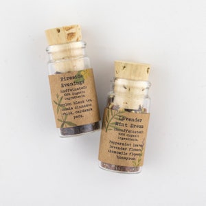 May include: Two small glass bottles with cork stoppers filled with loose leaf tea. The bottles have brown paper labels with the names of the teas: "Fireside Evenings" and "Lavender Mint Dream". The labels also list the ingredients and whether the tea is caffeinated or decaffeinated.
