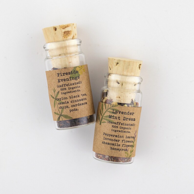 May include: Two small glass bottles with cork stoppers filled with loose leaf tea. The bottles have brown paper labels with the names of the teas: "Fireside Evenings" and "Lavender Mint Dream". The labels also list the ingredients and whether the tea is caffeinated or decaffeinated.