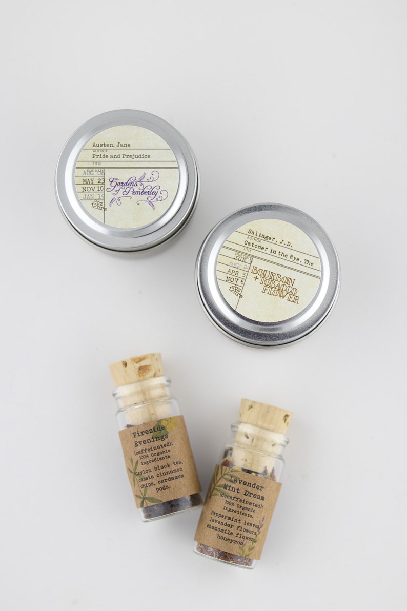 May include: Two silver tins with book titles and authors printed on the labels. The tins are labeled "Pride and Prejudice" by Jane Austen and "Catcher in the Rye, The" by J.D. Salinger. Two small glass bottles with cork tops contain loose leaf tea blends. The bottles are labeled "Fireside Evenings" and "Lavender Mint Dream".