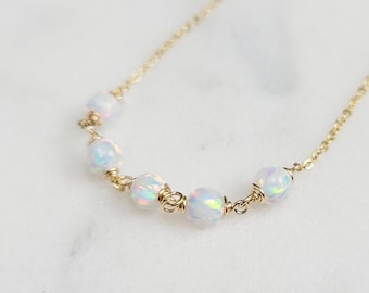 May include: A delicate gold chain necklace with a row of iridescent white opal beads.