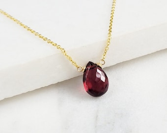 May include: A delicate gold chain necklace with a single teardrop-shaped red gemstone pendant.