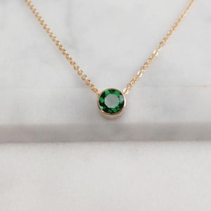 Puede incluir: Un delicado collar de cadena de oro con un pequeño colgante redondo de piedra preciosa verde.