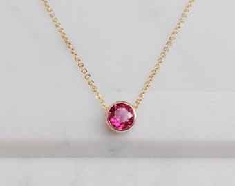 May include: A delicate gold chain necklace with a single round pink gemstone pendant.