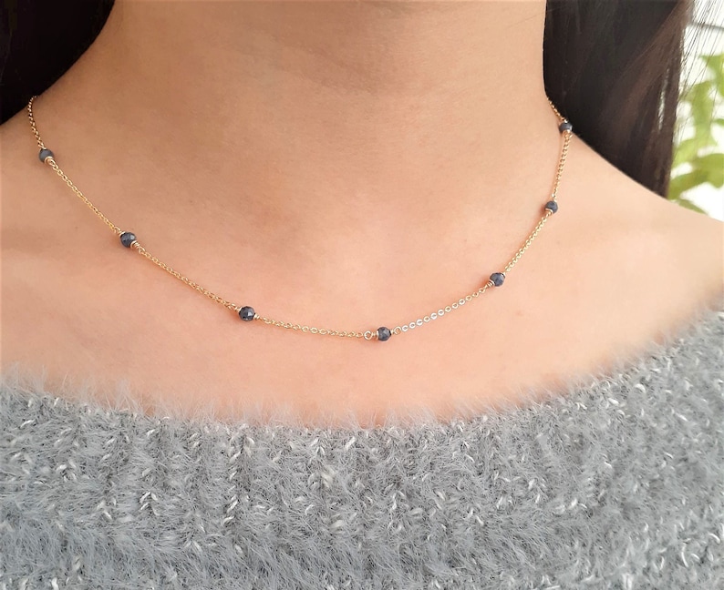 May include: A gold chain necklace with small, dark blue beads. The necklace is delicate and simple.