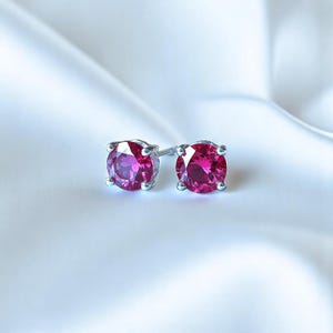 May include: A pair of silver stud earrings with round, bright pink gemstones.