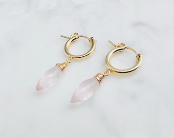 May include: A pair of gold hoop earrings with a pink quartz gemstone dangling from each hoop.