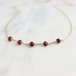 May include: A delicate gold chain necklace with four small, faceted, dark red gemstones.