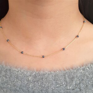 May include: A gold chain necklace with small blue beads. The necklace is delicate and simple.