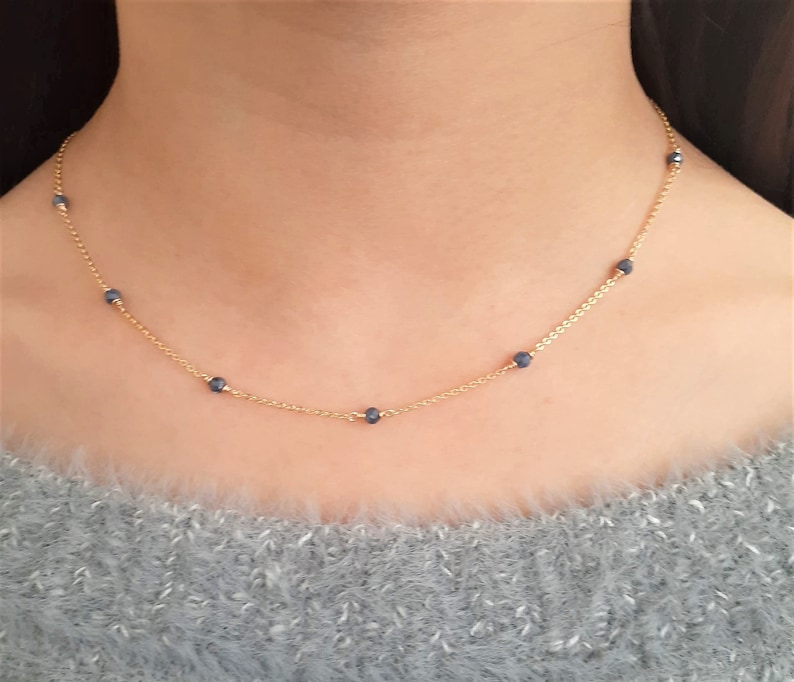 May include: A gold chain necklace with small blue beads. The necklace is delicate and simple.