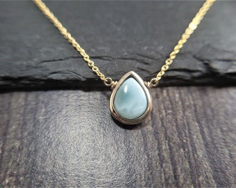 May include: A delicate gold chain necklace with a teardrop-shaped pendant featuring a light blue gemstone.