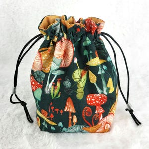 May include: A drawstring bag with a dark green background and a colorful mushroom print. The bag has a brown drawstring and is made of fabric.