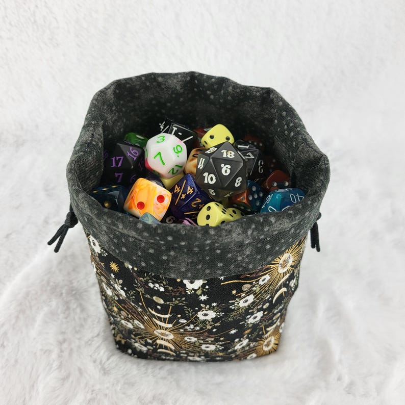 May include: A black fabric dice bag with a floral pattern and gold accents. The bag is filled with a variety of colorful dice.