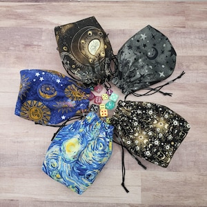 May include: Five drawstring dice bags with celestial and artistic designs. The bags feature patterns of moons, stars, and a Van Gogh-inspired print. Assorted dice are scattered around the bags, which are made of fabric.