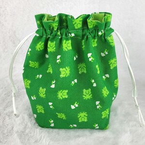May include: Green drawstring bag with a white frog and mushroom pattern. The bag has white drawstrings.