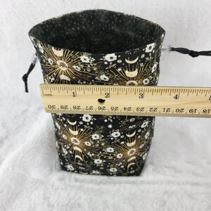 May include: Black fabric dice bag with a gold and white moon and star pattern. The bag is 3 inches tall and has a drawstring closure.