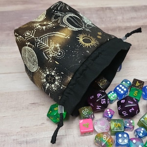 May include: A black drawstring dice bag with a celestial design in gold and white. The bag is open, spilling out a variety of colorful polyhedral dice. The dice are in various colors, including green, purple, and blue.