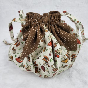 May include: A brown and white drawstring bag with a mushroom print. The bag has a brown polka dot fabric lining the top edge.