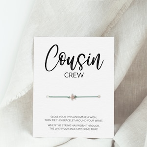 Op de afbeelding: Een witte kaart met de tekst "Cousin Crew" en een groen koordarmbandje met een zilveren sterbedel. De kaart bevat ook de tekst "Sluit je ogen en doe een wens, bind dan dit armbandje om je pols. Wanneer het koord versleten is, kan je wens uitkomen!"