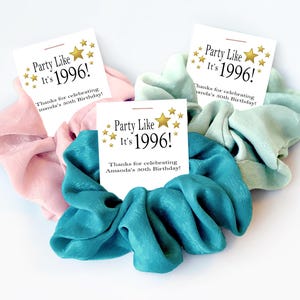 K&ouml;nnte beinhalten: Drei Haargummis in Rosa, T&uuml;rkis und Mintgr&uuml;n, jeweils mit einer wei&szlig;en Karte. Auf den Karten steht "Party Like It's 1996!" und sie feiern Amandas 30. Geburtstag. Ein lustiges, festliches Accessoire.