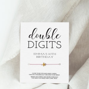 May include: A pink and gold bracelet with a star charm. The card reads "double digits Emma's 10th birthday" and includes instructions to make a wish and tie the bracelet around your wrist. When the string wears through, your wish may come true.