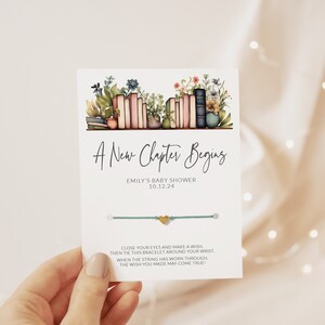 May include: A teal blue string bracelet with a gold heart charm. The card attached to the bracelet reads "A New Chapter Begins, Emily's Baby Shower, 10.12.24. Close your eyes and make a wish, then tie this bracelet around your wrist. When the string has worn through, the wish you made may come true!"
