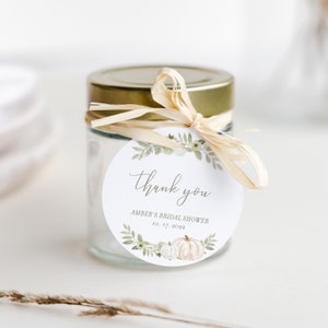 May include: A round, white thank you tag with green foliage and white pumpkins. The tag says "thank you" and "Amber's Bridal Shower 10.17.2022".