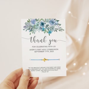 May include: A blue and white thank you card with a floral design. The card reads "Thank you for celebrating with us! Avery's First Holy Communion September 17th, 2023". The card also includes a blue string bracelet with a gold cross charm.