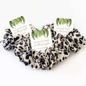 May include: Three jungle-themed party favor tags with the text "HALEYS LAST RUMBLE in the jungle" and a hashtag. The tags are placed on top of leopard print scrunchies.