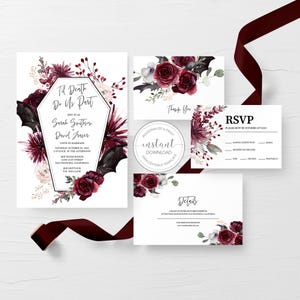 May include: A wedding invitation suite featuring a coffin-shaped frame, RSVP card, thank you card, and details card. The stationery is decorated with watercolor dark red roses, black bat wings, and foliage. A dark red ribbon is draped across.