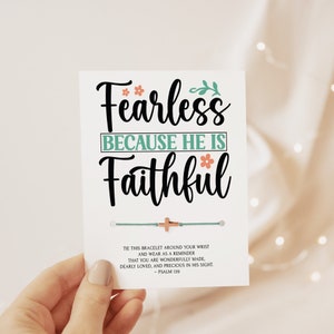 May include: A white card with the text "Fearless Because He Is Faithful" in black lettering with green and pink floral accents. The card also includes a blue and white string bracelet with a small gold cross charm. The text at the bottom of the card reads "Tie this bracelet around your wrist and wear as a reminder that you are wonderfully made, dearly loved, and precious in His sight - Psalm 139."