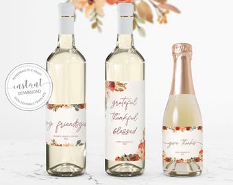 May include: Three glass bottles with white labels featuring watercolor floral and pumpkin designs. The labels include the text "friendsgiving," "grateful thankful blessed," and "give thanks" in a script font with autumn-themed illustrations.