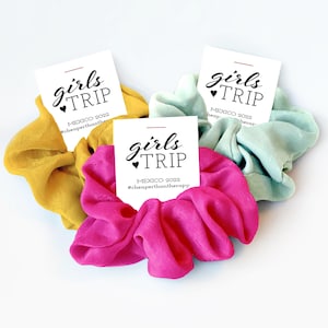 May include: Three fabric hair scrunchies in mustard yellow, bright pink, and light mint green. Each scrunchie is attached to a white card featuring the black text girls TRIP, MEXICO 2022, and the hashtag #cheaperthantherapy.