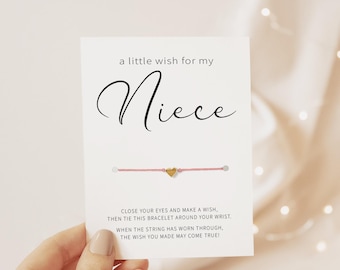May include: A white rectangular card featuring the text a little wish for my Niece and a pink string bracelet with a small gold heart charm. The card includes instructions to close your eyes, make a wish, and tie the bracelet on.