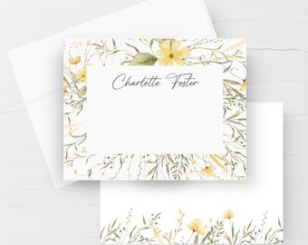 Puede incluir: Una tarjeta de papelería rectangular blanca con un borde de acuarela de flores silvestres amarillas y follaje verde, con el nombre Charlotte Foster impreso en letra cursiva negra en el centro, junto a un sobre a juego.