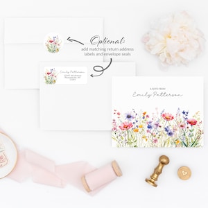 May include: A white envelope with a floral sticker and a return address label. The envelope is next to a card with a watercolor painting of wildflowers and the text "A NOTE FROM Emily Patterson".