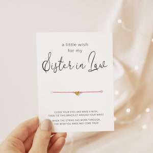 Op de afbeelding: Een roze koordarmband met een gouden hartbedel. De kaart luidt: "Een klein wensje voor mijn schoonzuster. Sluit je ogen en doe een wens, bind dan deze armband om je pols. Wanneer het koord versleten is, kan je wens uitkomen!"