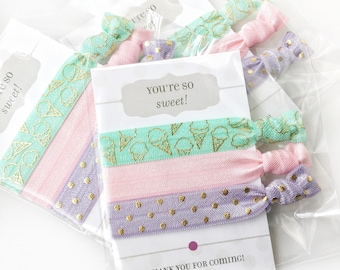 May include: Three elastic hair ties on a white card labeled you're so sweet! and THANK YOU FOR COMING!. The ties feature a mint green ice cream cone pattern, a solid light pink, and a lavender purple with gold polka dots, all in clear packaging.