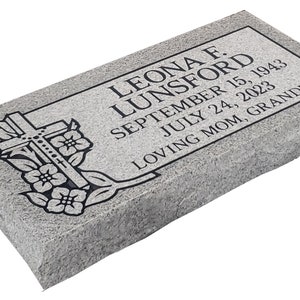 May include: A gray granite headstone with a black cross and floral design. The inscription reads "Leona F. Lunsford, September 15, 1943, July 24, 2023, Loving Mom, Grandma."