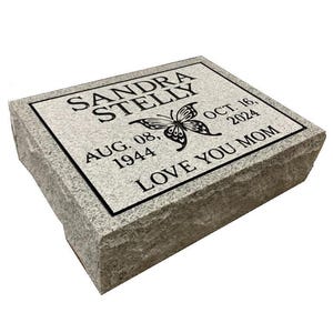 May include: A gray granite headstone with a black inscription that reads "SANDRA STELLY AUG. 08, 1944 OCT. 16, 2024 LOVE YOU MOM". A black butterfly is engraved on the headstone.