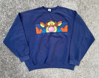 May include: A navy blue sweatshirt with a cartoon image of Tigger from Winnie the Pooh. Tigger is blowing a pink bubble and the text "TIGGER" is printed below the image.