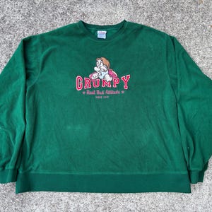 May include: A green sweatshirt with a graphic of the Grumpy character from Snow White. The design includes the word "GRUMPY" in red, and the text "Real Bad Attitude Since 1937".