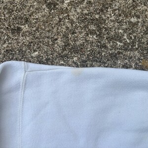 May include: Close-up of a white sweatshirt with a small, light brown stain on the sleeve.