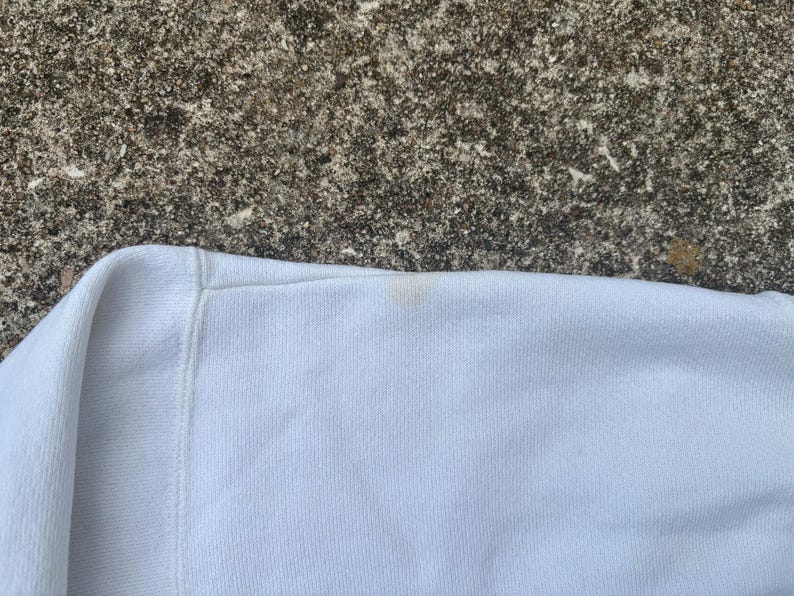 May include: Close-up of a white sweatshirt with a small, light brown stain on the sleeve.