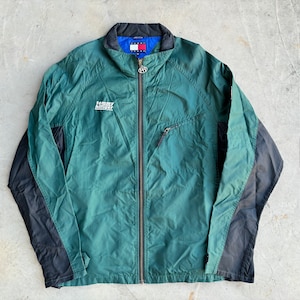 May include: Green and black Tommy Hilfiger jacket with a full zipper. The jacket has a black collar and a small logo on the chest. The Tommy Hilfiger logo is also visible on the collar. The jacket is made of a lightweight material.