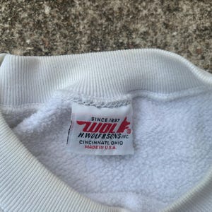 May include: White sweatshirt with a red and white label that reads "Since 1987 Wolf H. Wolf & Sons Inc. Cincinnati Ohio Made in U.S.A."
